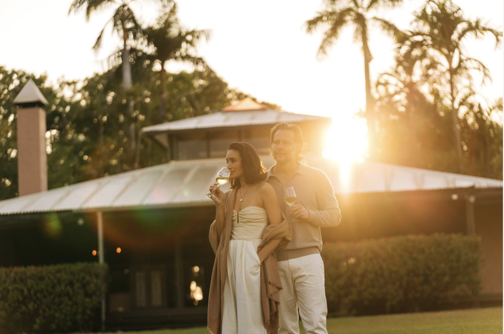 A couple stands together on manicured grounds during golden hour, with a modern luxury resort