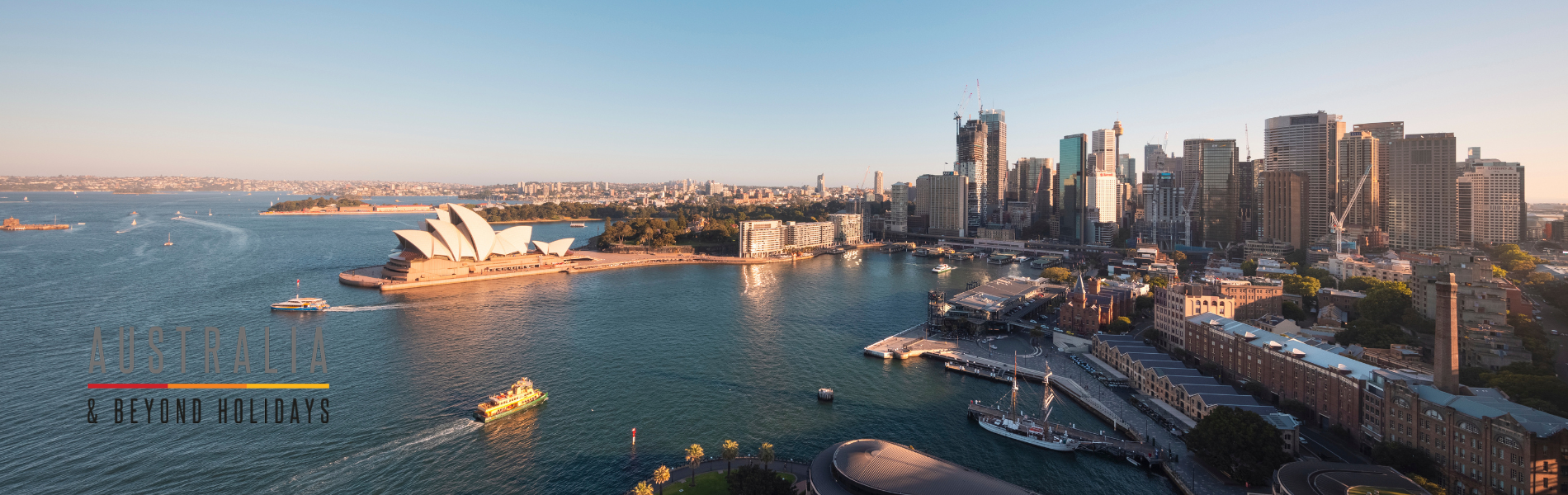 A stunning aerial photograph of Sydney Harbour featuring the iconic Sydney Opera House, the central business district skyline, and surrounding waterfront areas bathed in golden afternoon light. The image captures the architectural beauty and natural harbor setting that define Australia's most recognizable city.