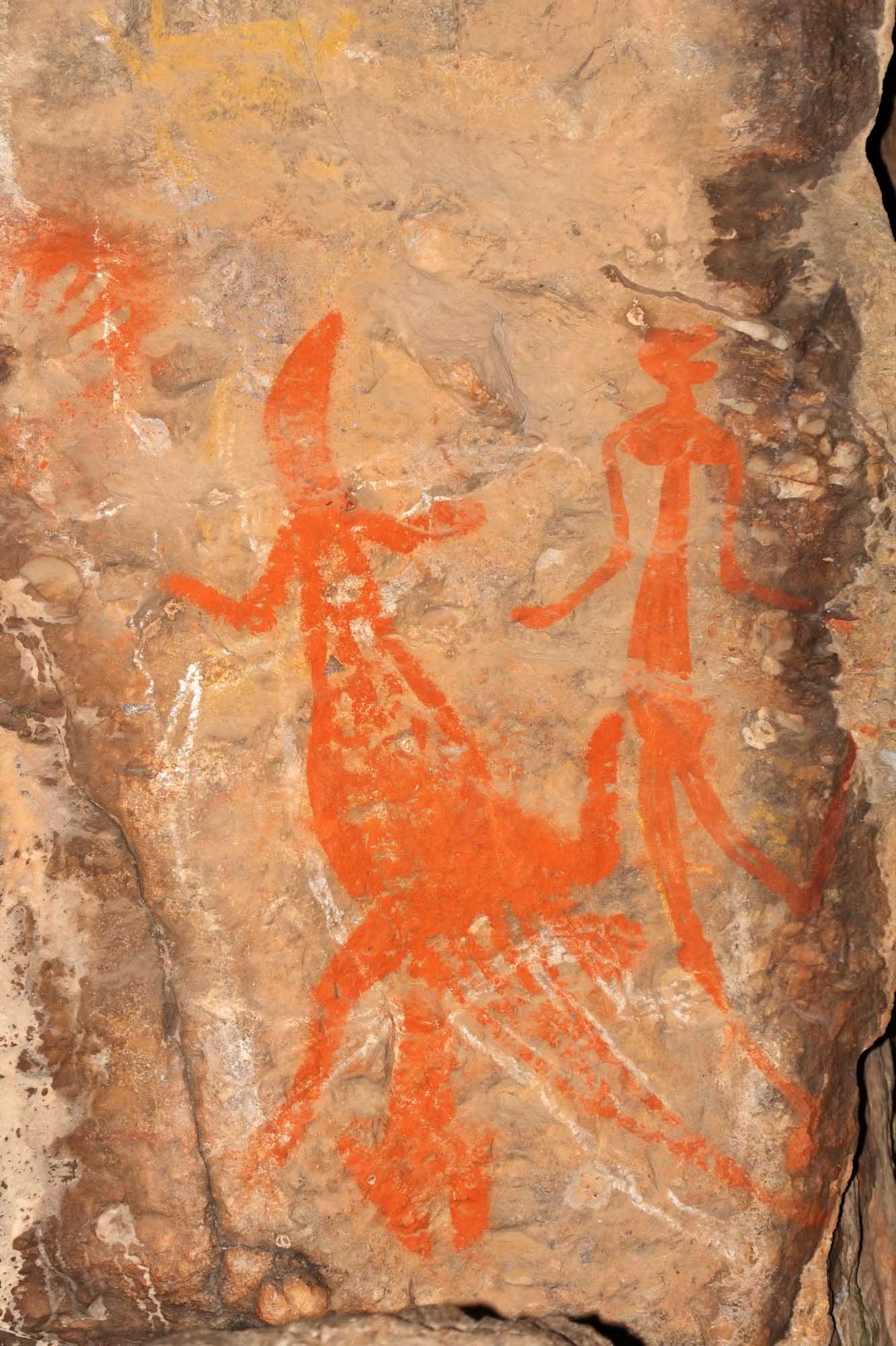 Ancient Aboriginal rock art paintings in vibrant ochre-red depicting human and animal figures on a weathered sandstone rock face at Nourlangie in Kakadu National Park. The distinctive stick-figure style and natural pigmentation exemplify the rich indigenous artistic heritage of Northern Australia.