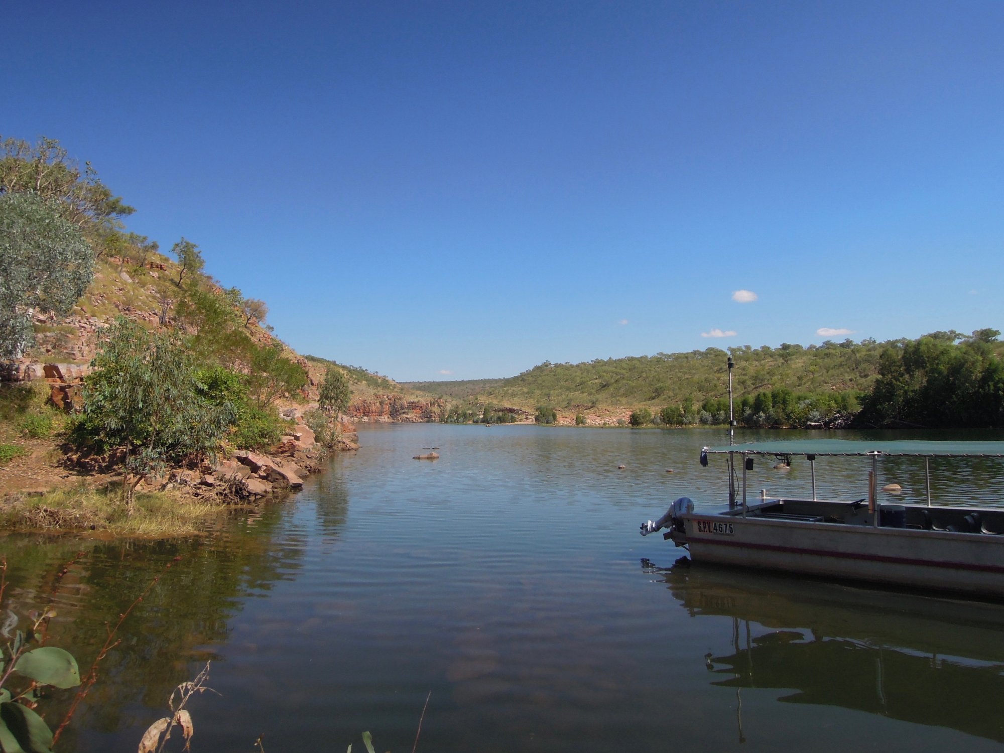 A serene river landscape featuring a moored expedition boat on calm waters, with red sandstone