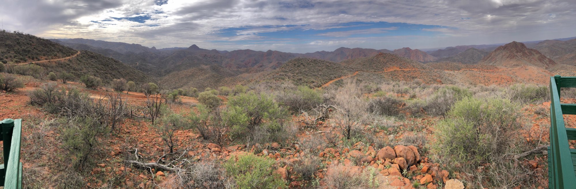 Flinders Ranges Mountain Vista Australia A panoramic landscape view of the rugged Flinders Ranges in South Australia, featuring rolling mountains, red earth, sparse vegetation, and dramatic cloudy skies. The vista showcases the semi-arid terrain with scattered shrubs and trees characteristic of this UNESCO World Heritage region.