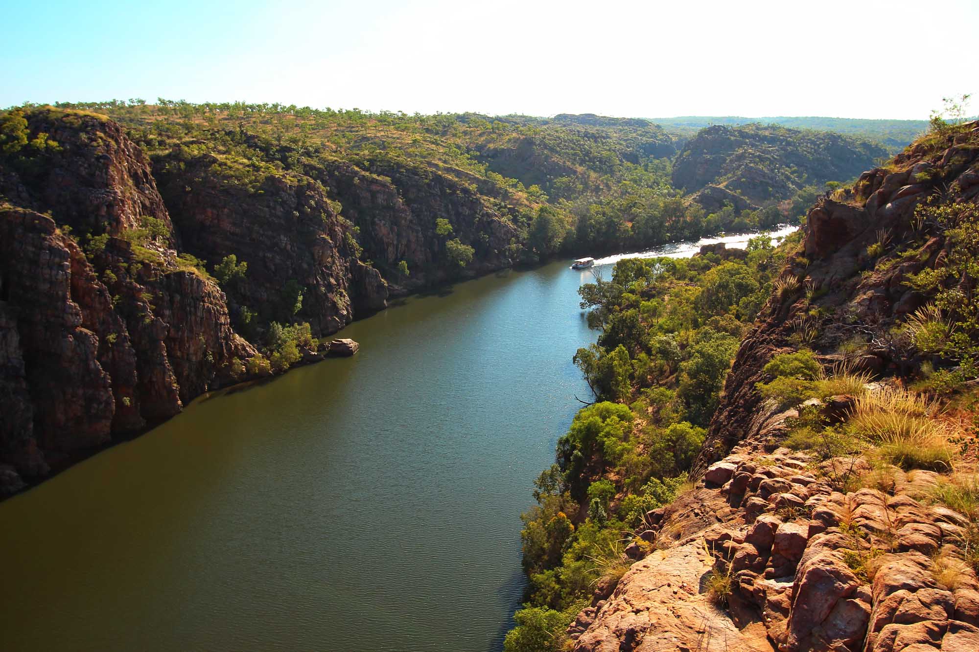 A stunning aerial view of Katherine Gorge in Australia's Northern Territory, featuring dramatic red sandstone cliffs towering above the winding turquoise river, surrounded by lush eucalyptus woodland and tropical vegetation.