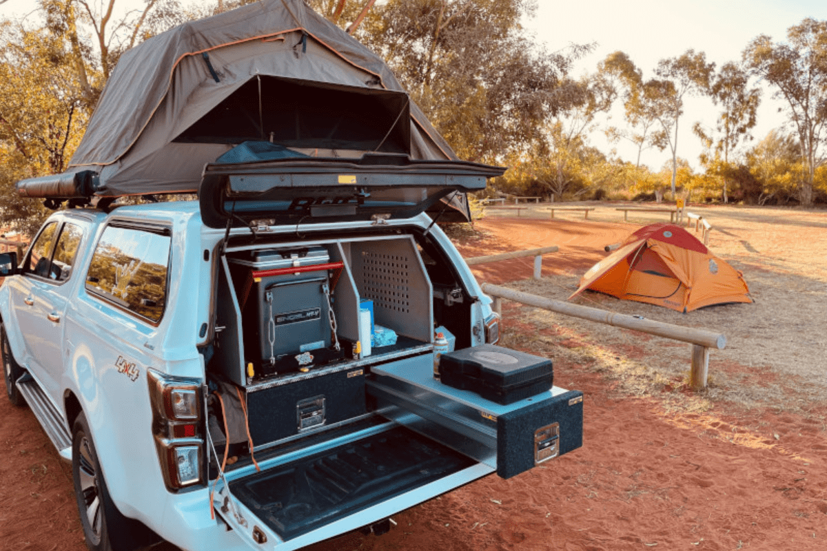 A light blue pickup truck equipped with a rooftop tent is set up at a desert campground, with