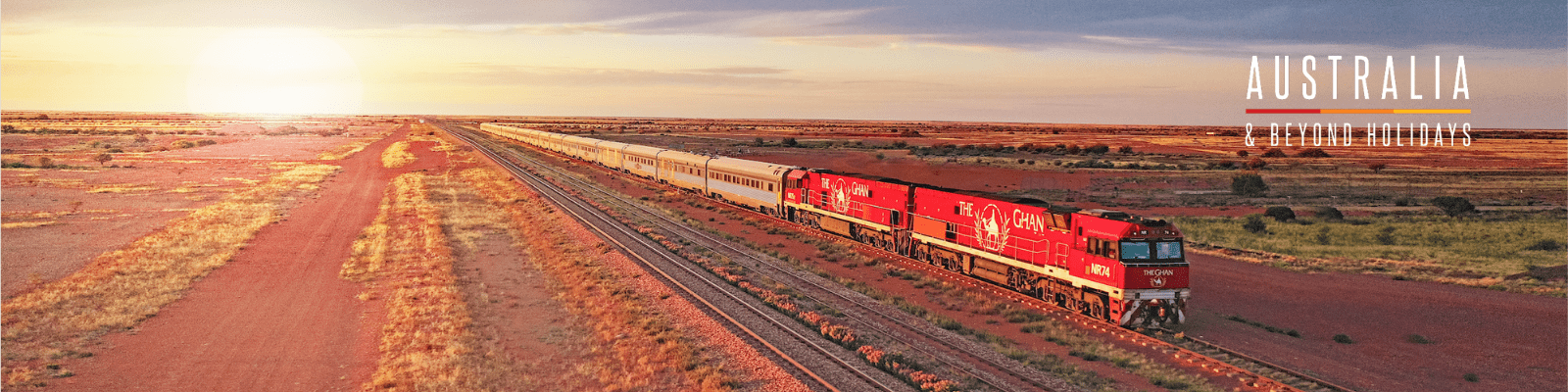 A luxury passenger train with distinctive red locomotives travels through the vast, arid Australian Outback at sunset, with red earth and sparse vegetation stretching to the horizon under golden light.