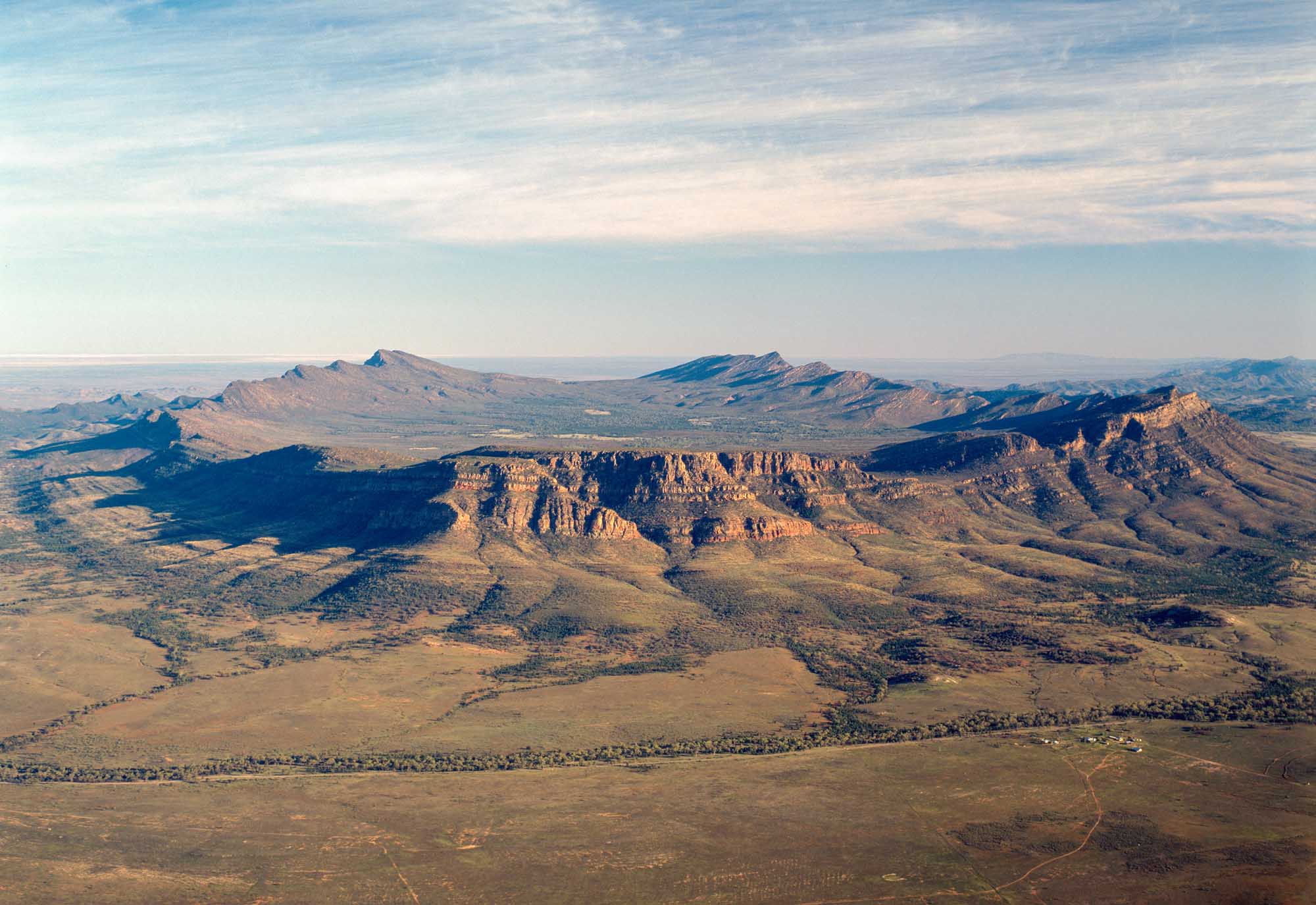 An aerial photograph of Wilpena Pound, a prominent natural amphitheater of rugged mountains and ridges in South Australia's Flinders Ranges. The distinctive layered rock formations and surrounding semi-arid landscape showcase the dramatic geological features of this iconic Australian destination.