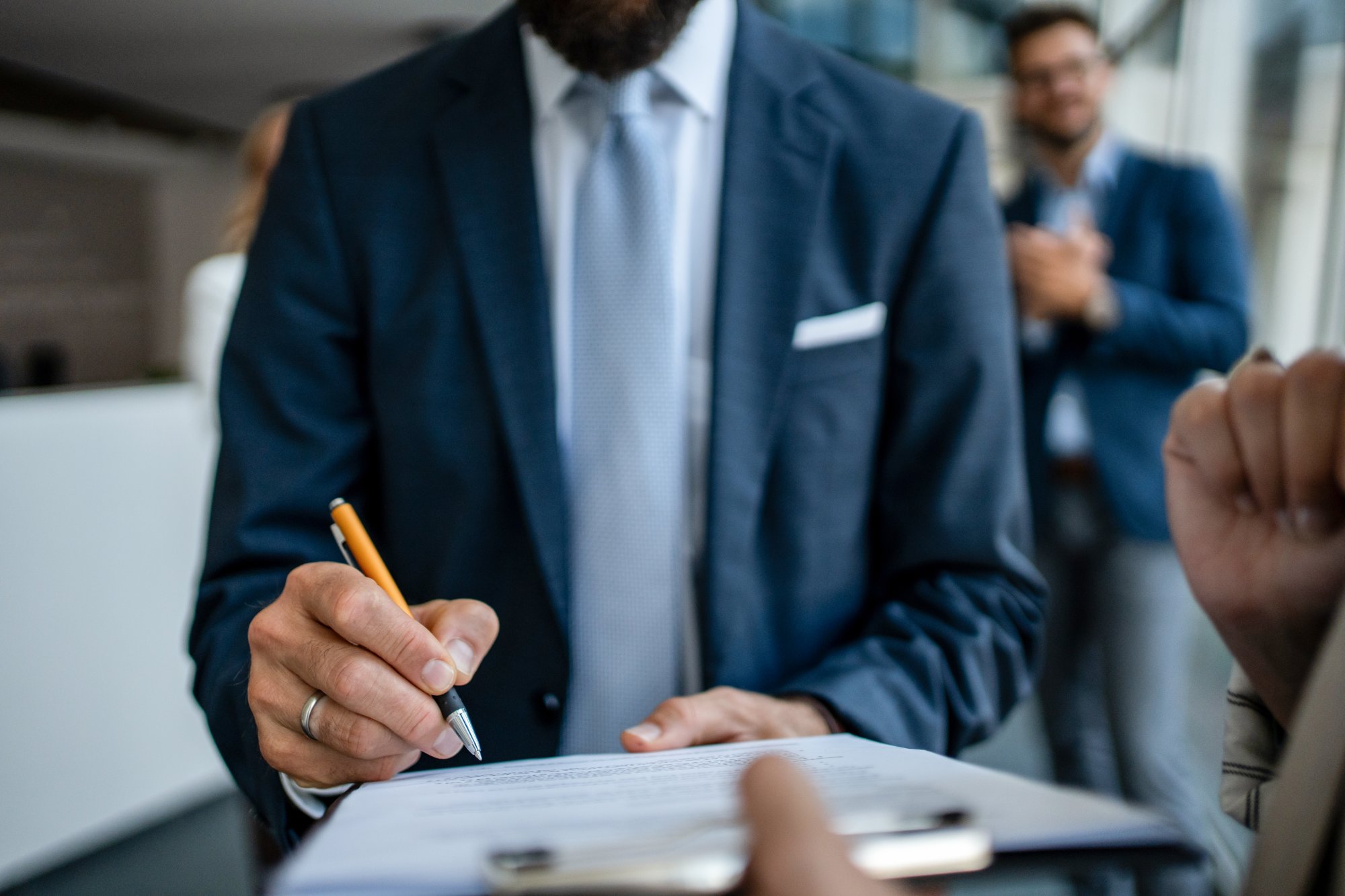 Business Professional Signing Document A well-dressed businessman in a navy blazer and light blue shirt holds a pen and signs a document