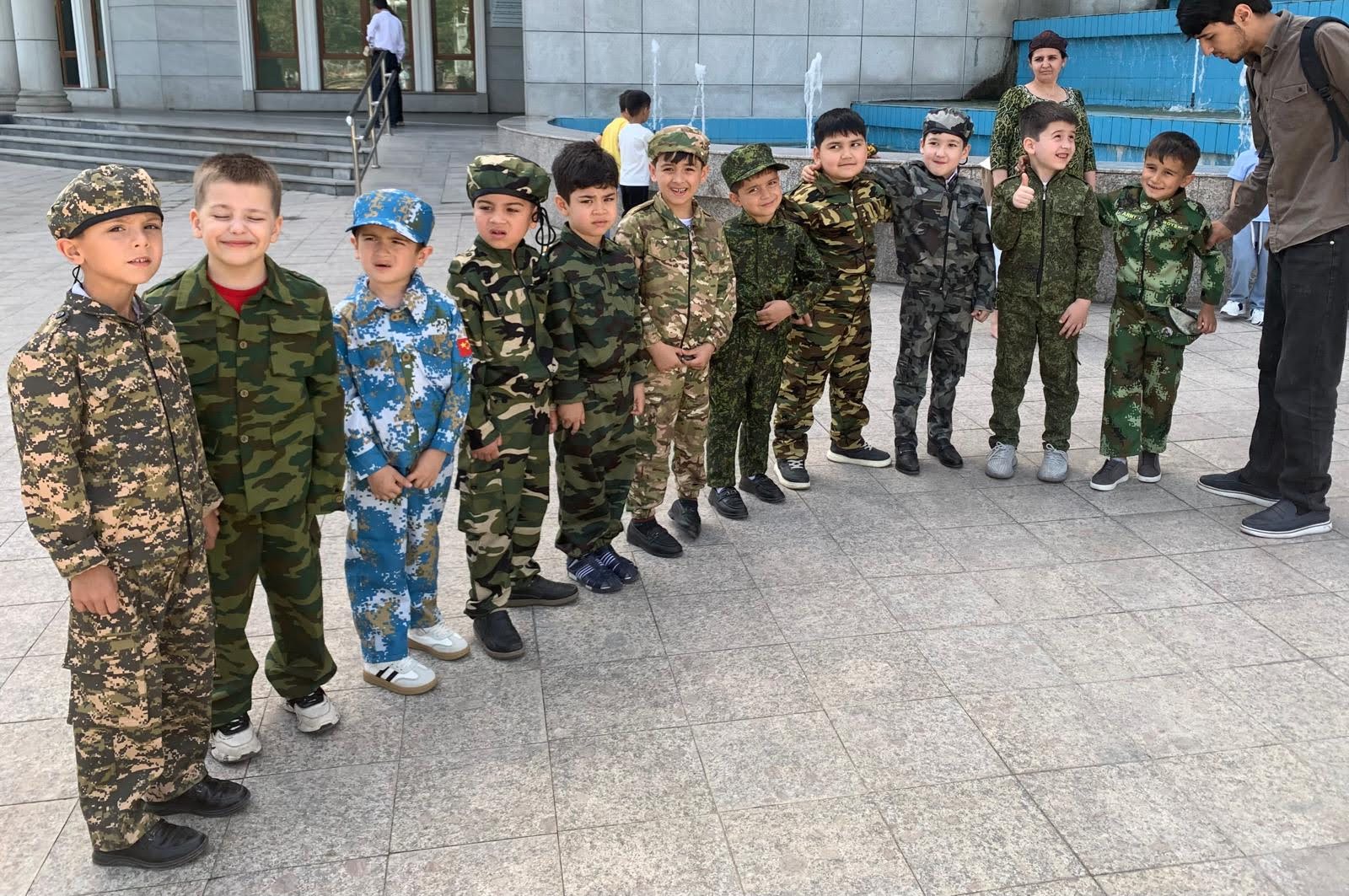 A group of young children wearing various military-style camouflage uniforms and caps stand in