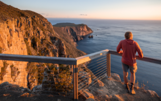 A jogger in a burgundy hoodie runs along a clifftop trail at golden hour, overlooking dramatic