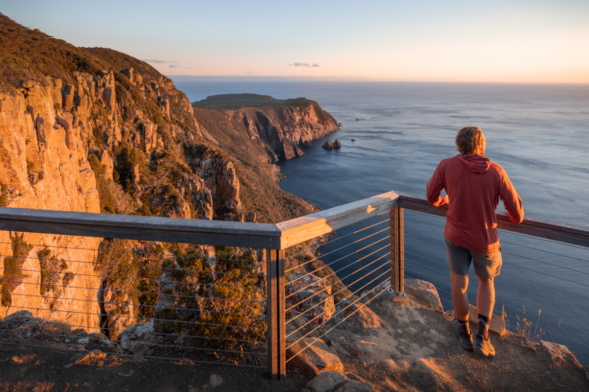 Coastal Cliff Runner at Sunrise A jogger in a burgundy hoodie runs along a clifftop trail at golden hour, overlooking dramatic