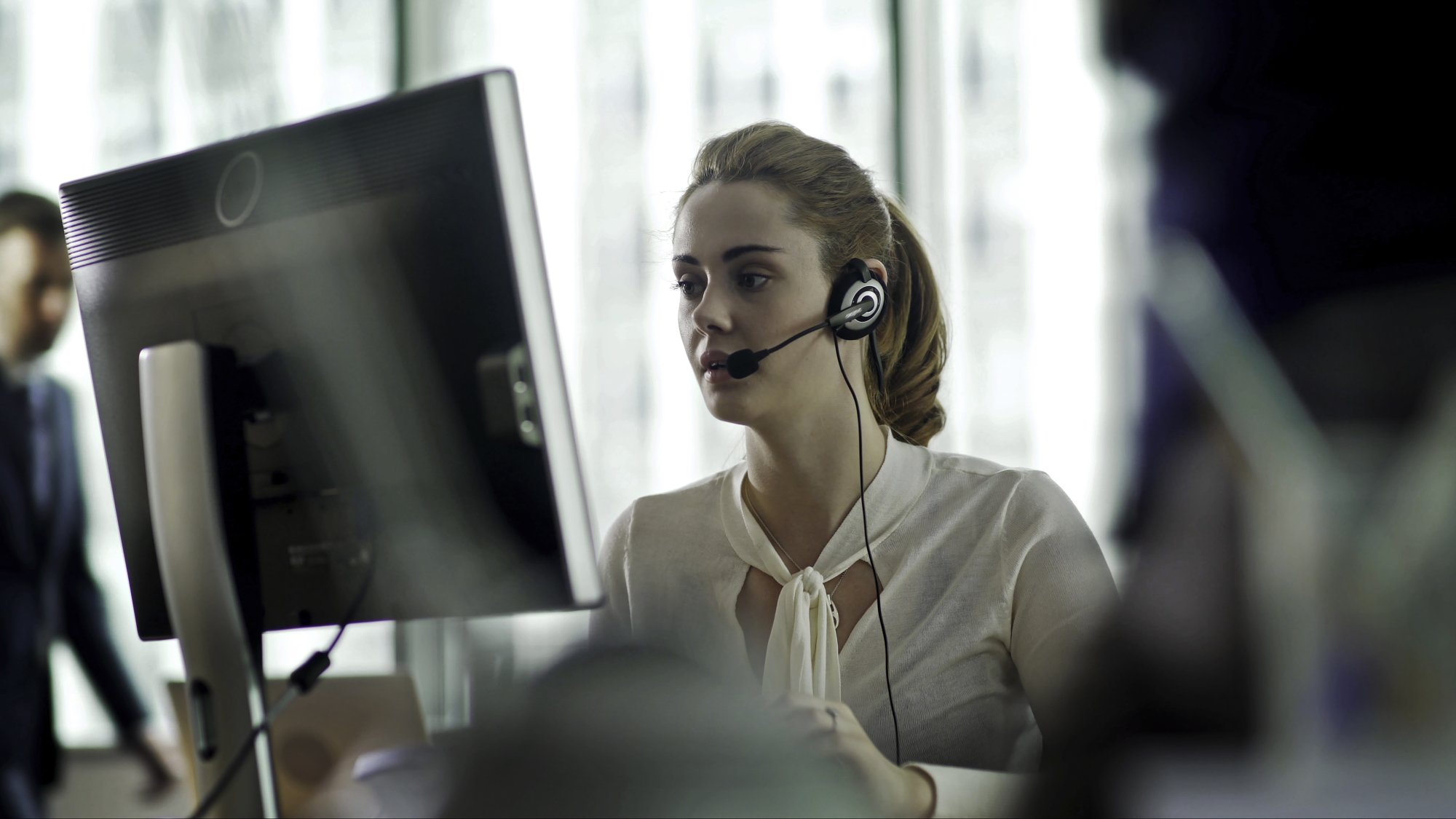 A professional woman wearing a white blouse sits at a computer workstation in a modern office