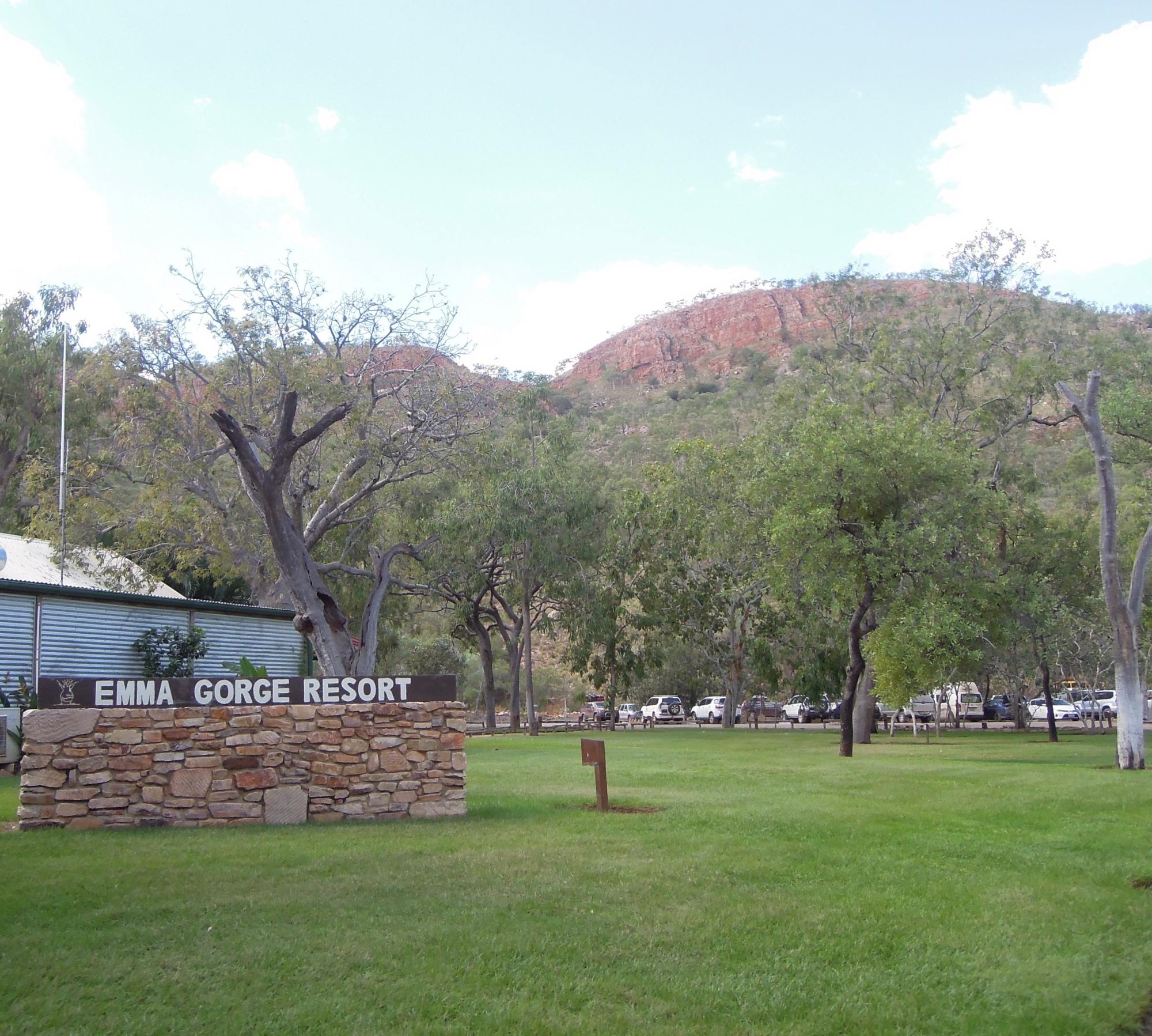 The entrance sign for Emma Gorge Resort set against a lush green lawn with large eucalyptus trees