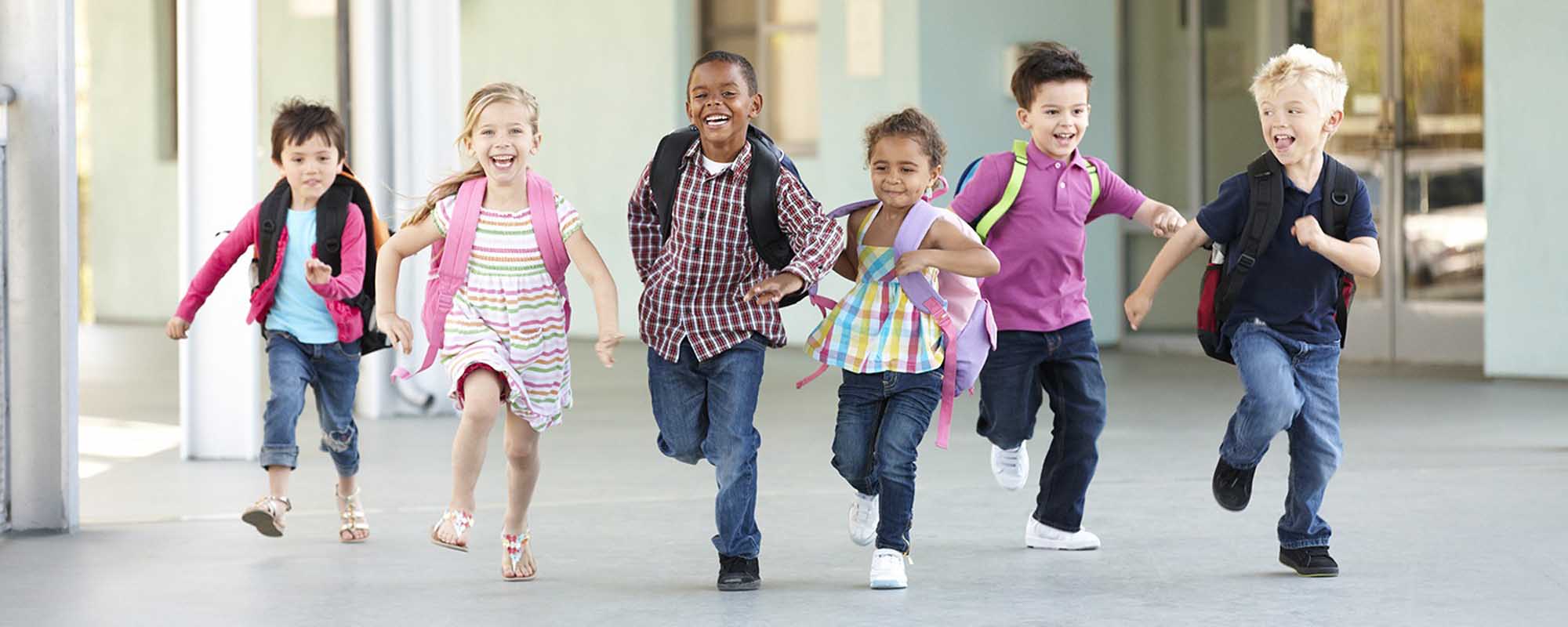 A diverse group of six elementary school-aged children running together down a bright, modern