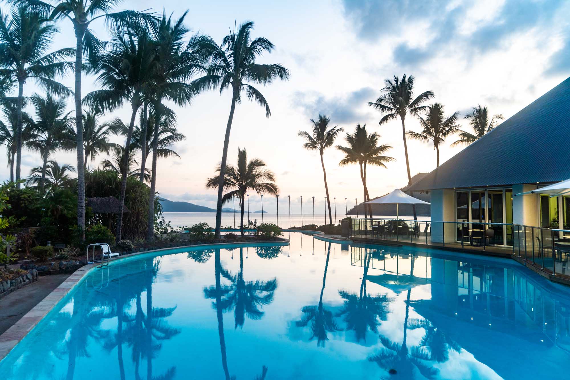 A stunning infinity pool at a tropical resort overlooking a pristine bay, with swaying palm trees