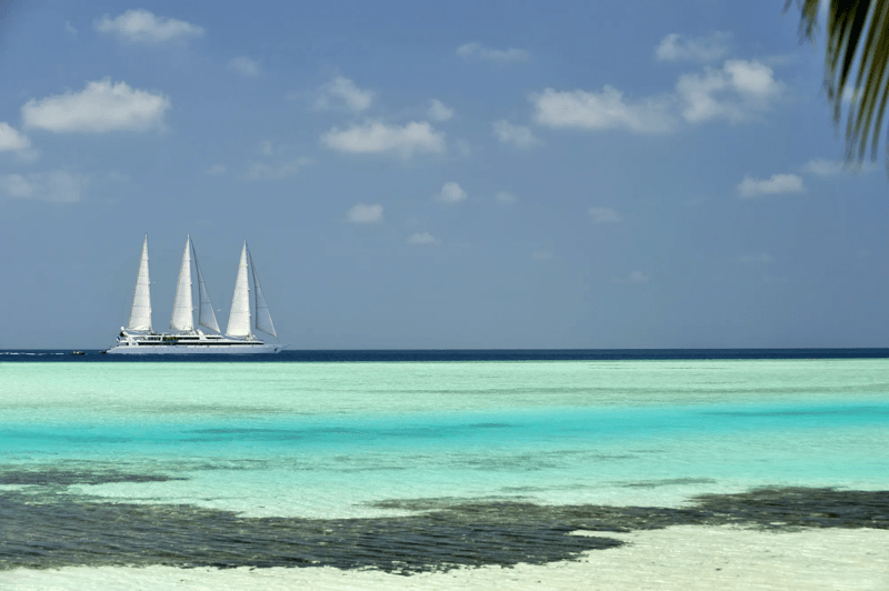 A pristine white multi-masted sailing yacht anchors in the crystalline turquoise waters of