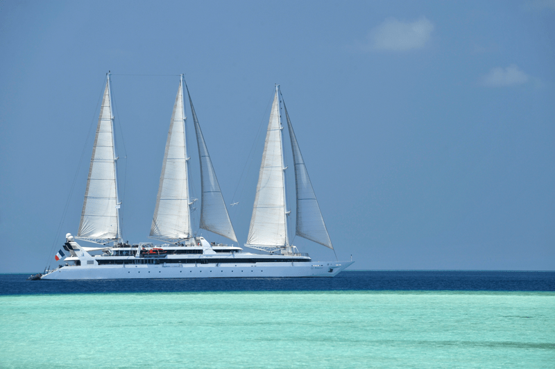 A magnificent three-masted sailing yacht with billowing white sails anchors in crystalline