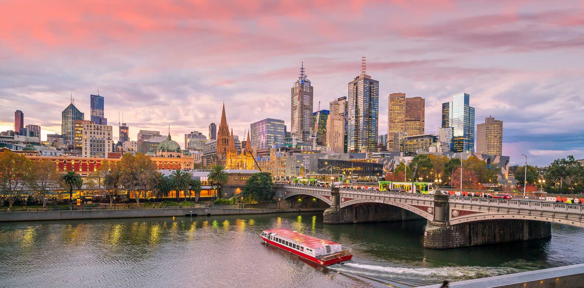 A panoramic view of Melbourne's iconic skyline at dusk, featuring illuminated skyscrapers, historic