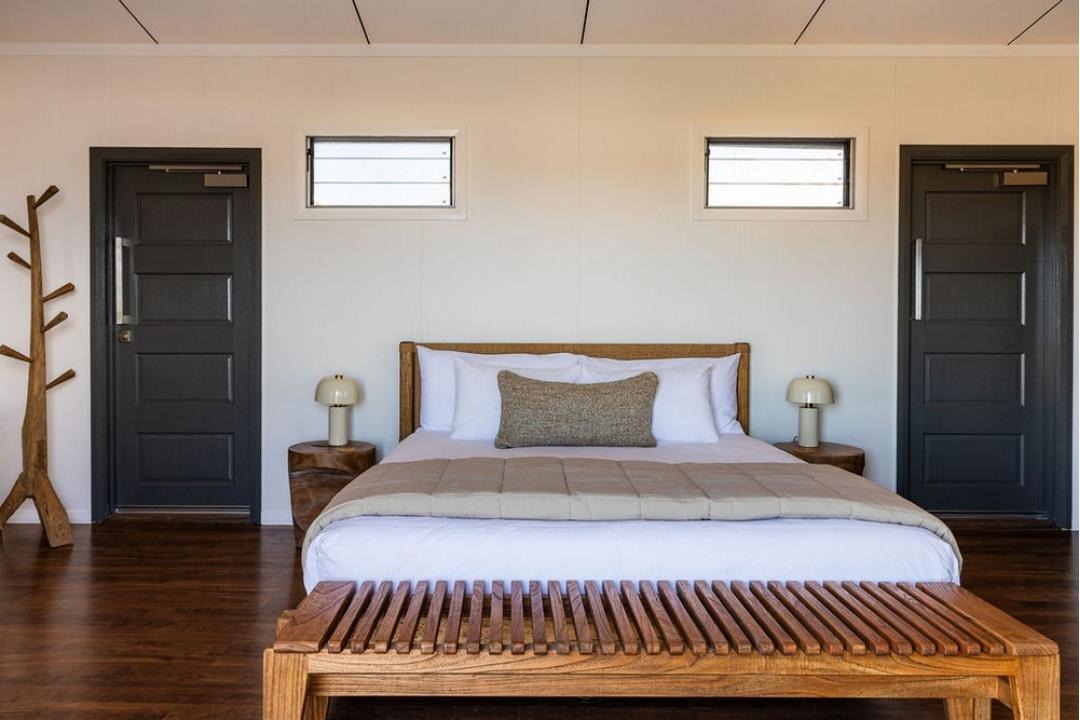 A contemporary bedroom featuring a wooden-framed bed with neutral bedding, symmetrical nightstands