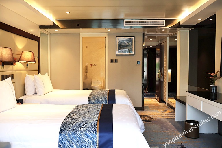A contemporary cruise ship stateroom featuring two queen beds with decorative blue patterned