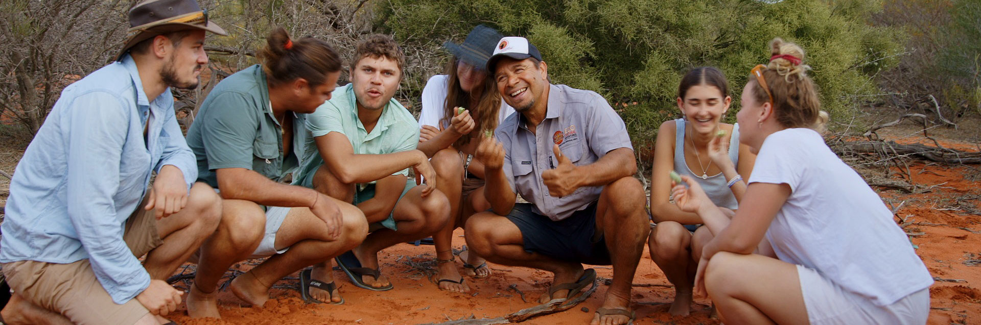 A diverse group of people gathered in a circle on red earth during an outdoor team-building