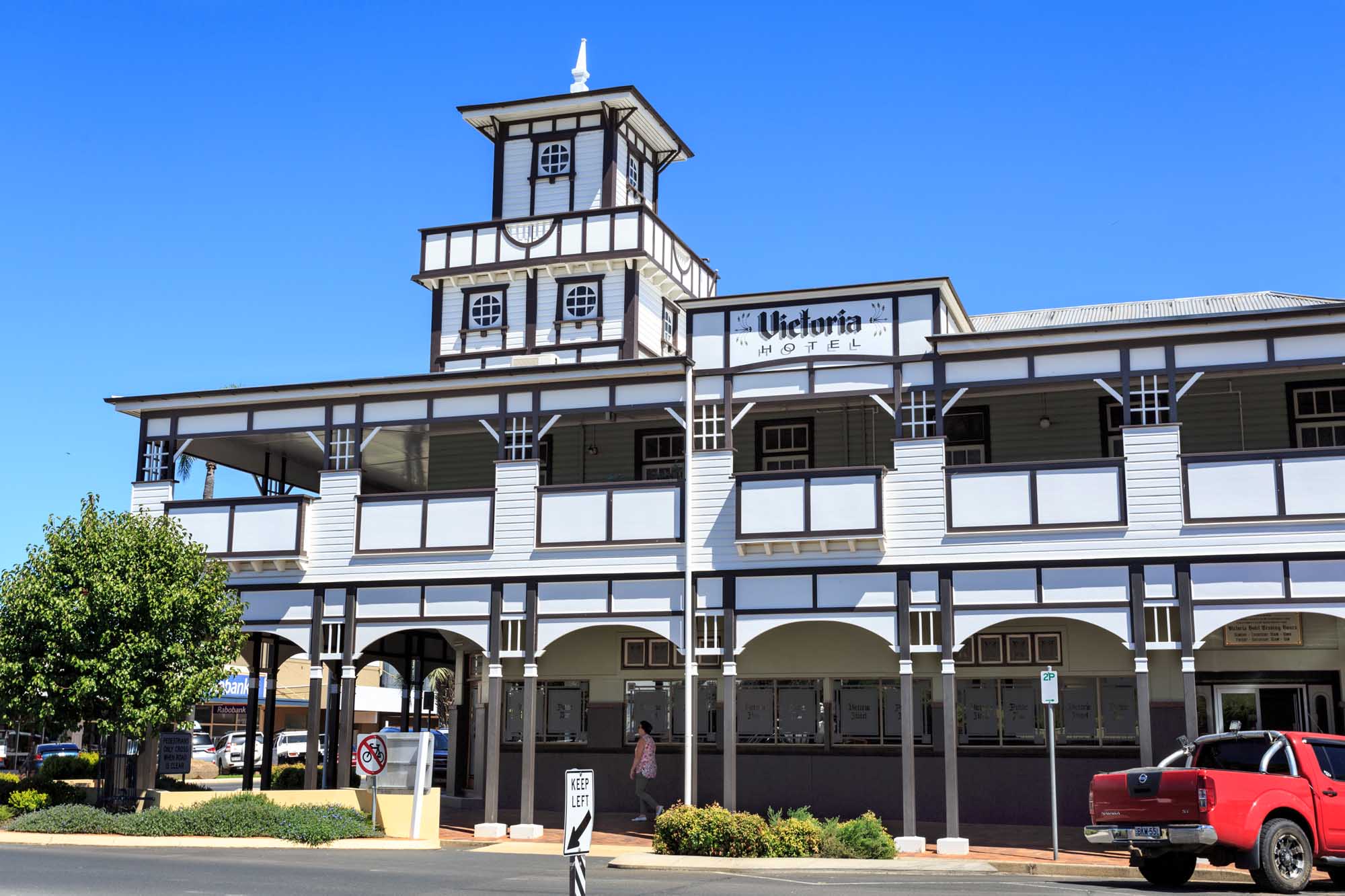 The iconic Victoria Hotel is a historic brick and timber building featuring distinctive dark panelling with white lattice work, ornamental stained glass windows, and a prominent decorative tower. Located in Goondiwindi, Queensland, this charming colonial-era structure exemplifies classic Australian country town architecture with its multi-story veranda and period detailing.