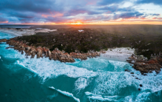 A dramatic aerial view of the Bay of Fires in Tasmania, featuring turquoise waters