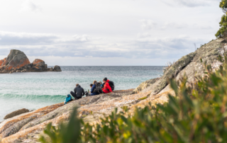 A group of travelers sit on rocky granite outcrops overlooking the turquoise waters and distinctive