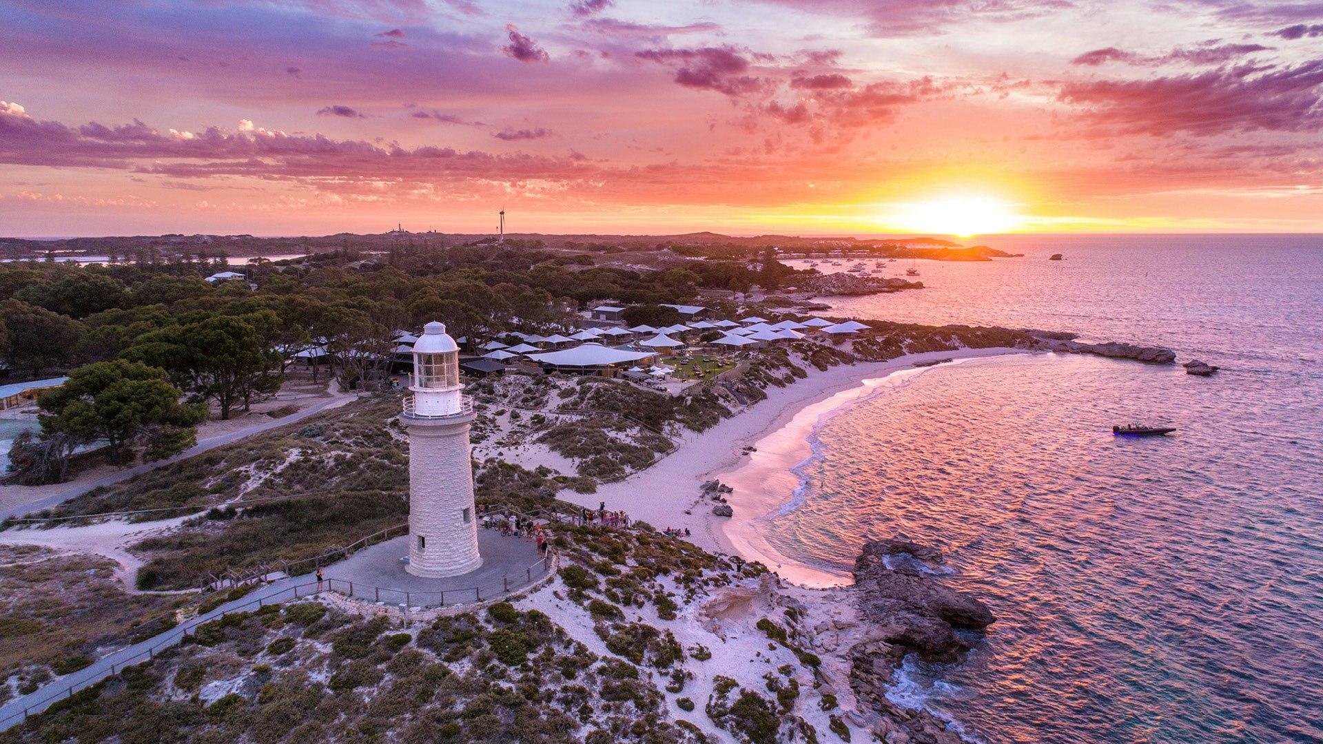 Coastal Lighthouse at Sunset A picturesque white lighthouse stands prominently on a rocky headland overlooking a crescent sandy