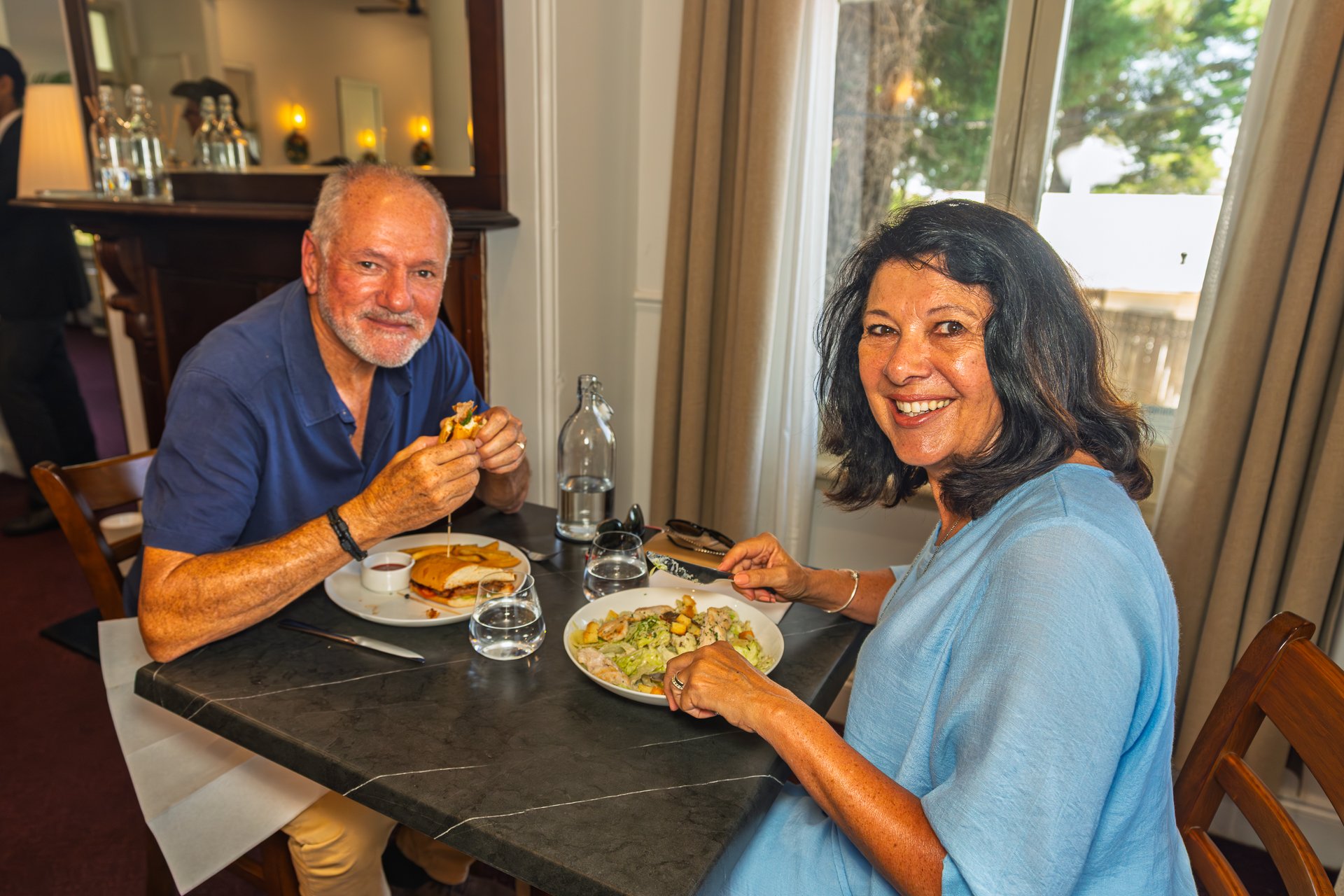 A smiling couple dines together at a black marble table in a sophisticated, well-lit dining room