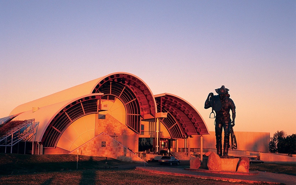 A silhouetted cyclist stands with their bike in front of the distinctive curved architectural