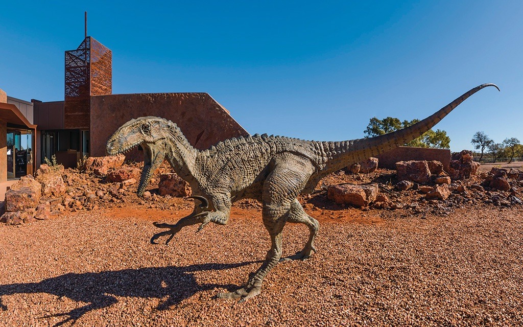 A detailed dinosaur sculpture, appearing to be a theropod with an extended tail, positioned in