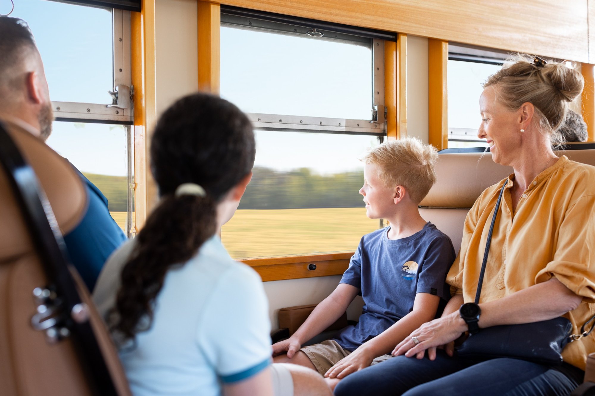 Family Enjoying Scenic Coach Tour through Countryside A woman and young boy sit together on a coach bus with large windows, enjoying views of rolling