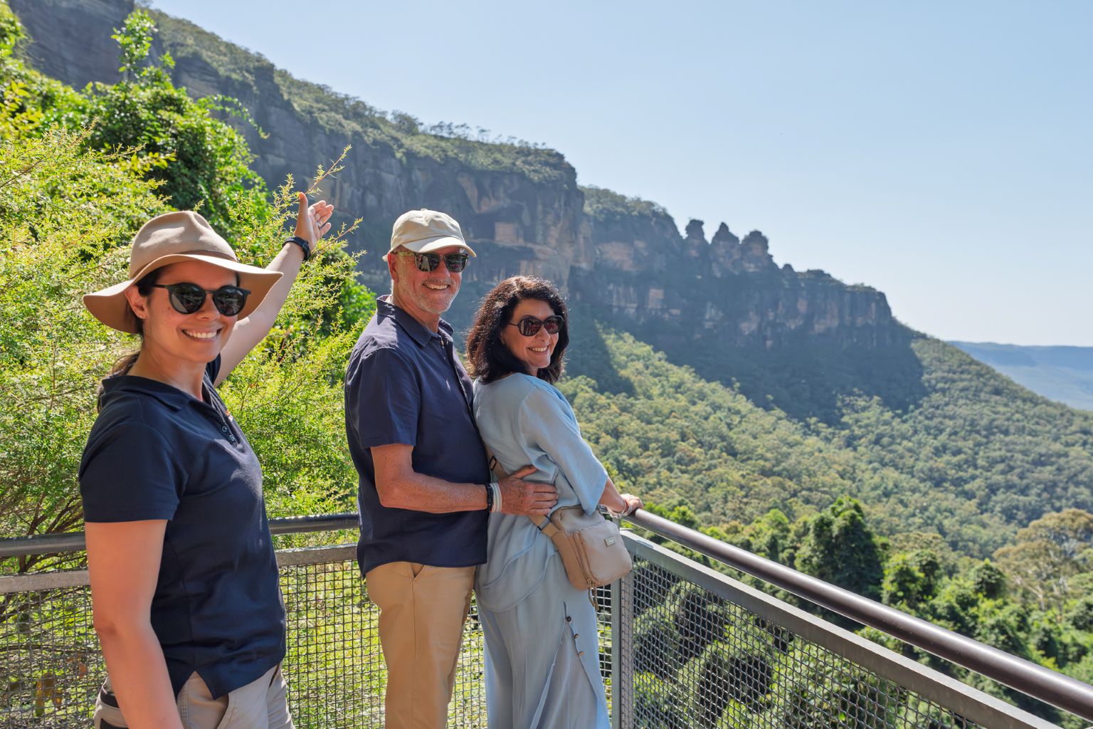Three visitors pose together at a scenic overlook in the Blue Mountains, smiling at the camera