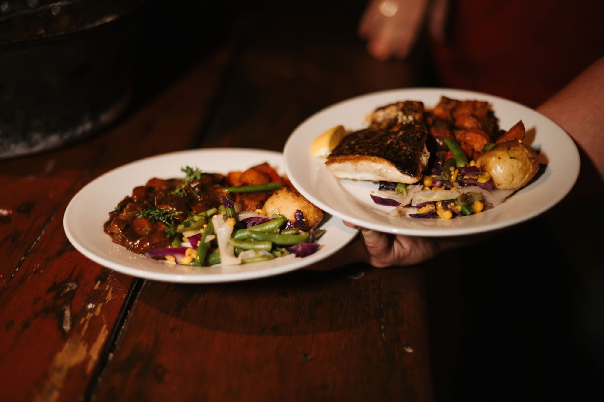 Two elegantly plated dishes featuring seared fish with crispy skin, roasted potatoes, and colorful