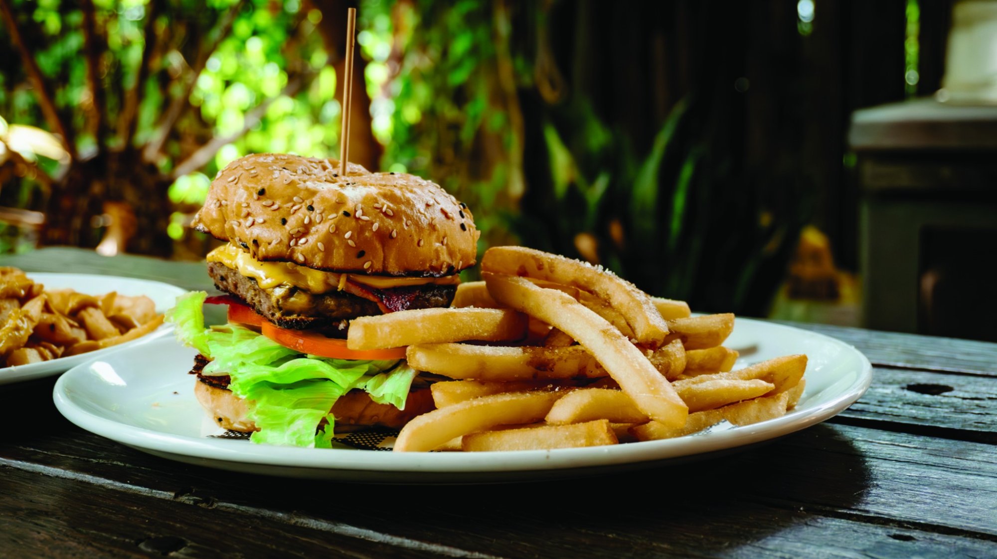 A beautifully plated gourmet burger on a seeded bun with fresh lettuce and tomato, accompanied by