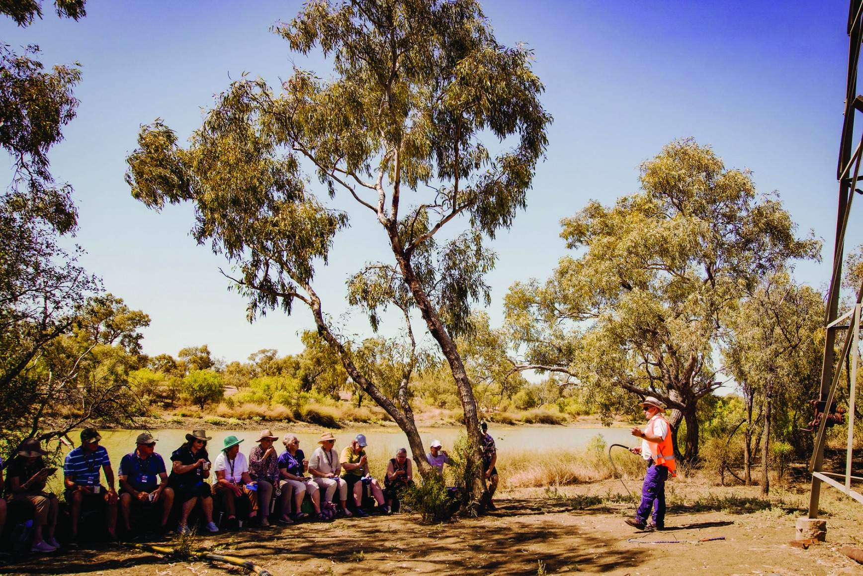 A group of Indigenous Australian community members gather in the shade of eucalyptus trees along