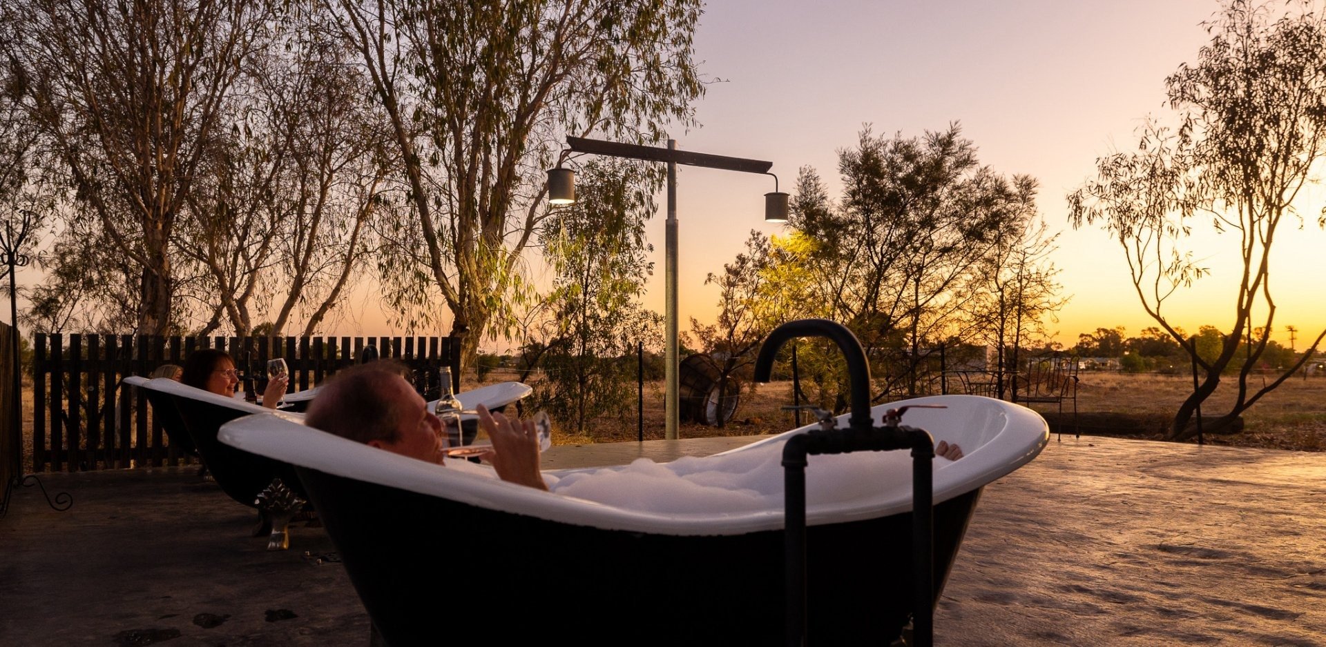 A person relaxes in a luxurious black and white freestanding bathtub positioned in an outdoor