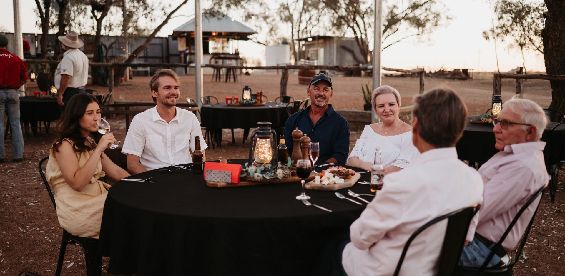 A group of six adults enjoy an elegant dinner around a black-draped table in an arid