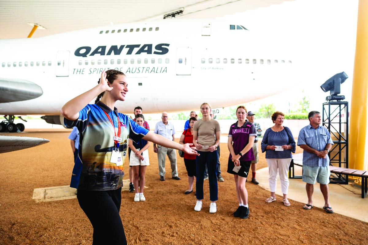 A Qantas Airways staff member conducts an educational tour for visitors beneath a large Boeing 747