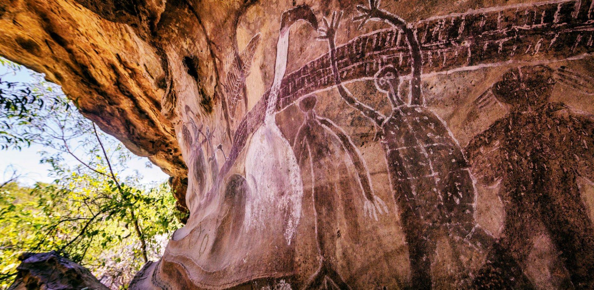 Ancient Aboriginal rock art carvings depicting human and animal figures on a weathered sandstone