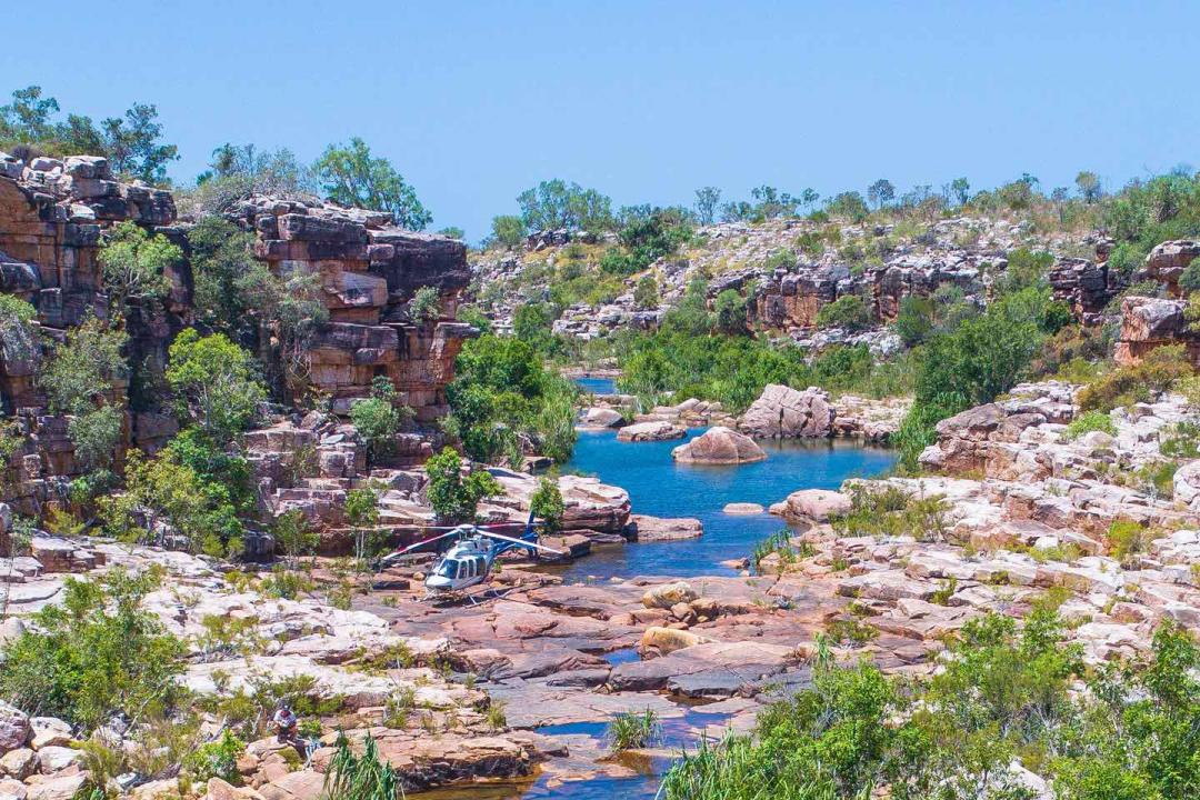 A scenic rocky gorge landscape featuring vibrant blue waterholes nestled between red sandstone