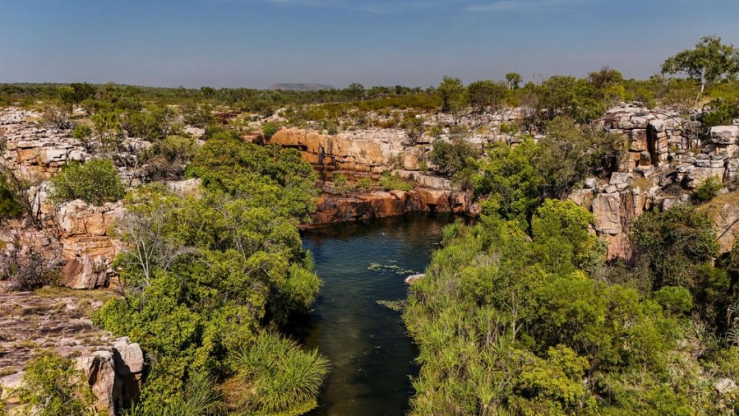 A scenic aerial view of a dramatic rocky gorge featuring a pristine blue waterhole surrounded