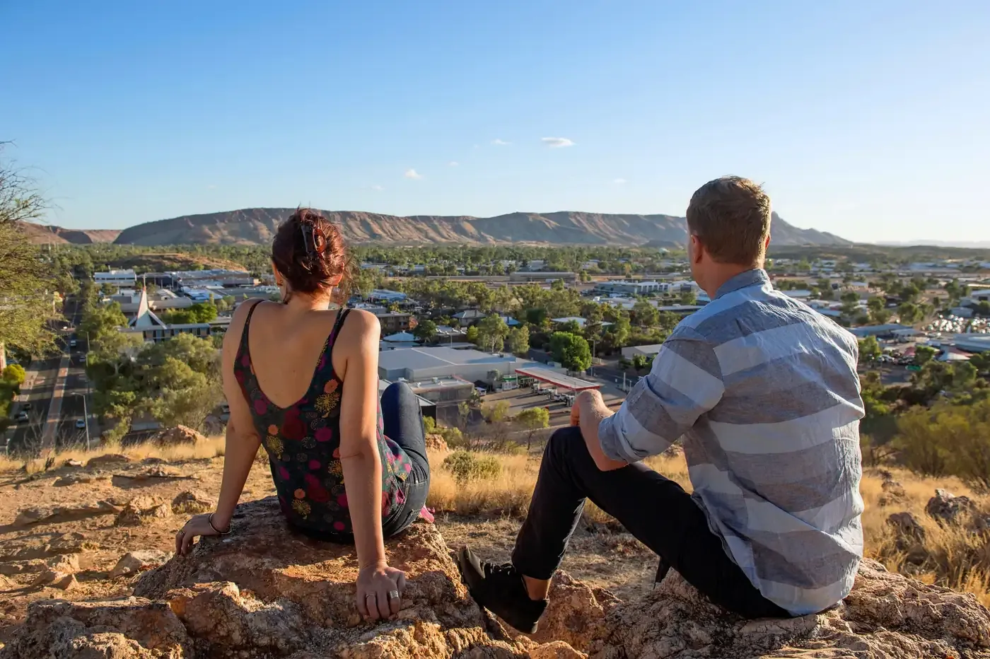 Scenic Overlook of Outback Town and Ranges Two tourists enjoy a panoramic view from a elevated vantage point overlooking a sprawling outback