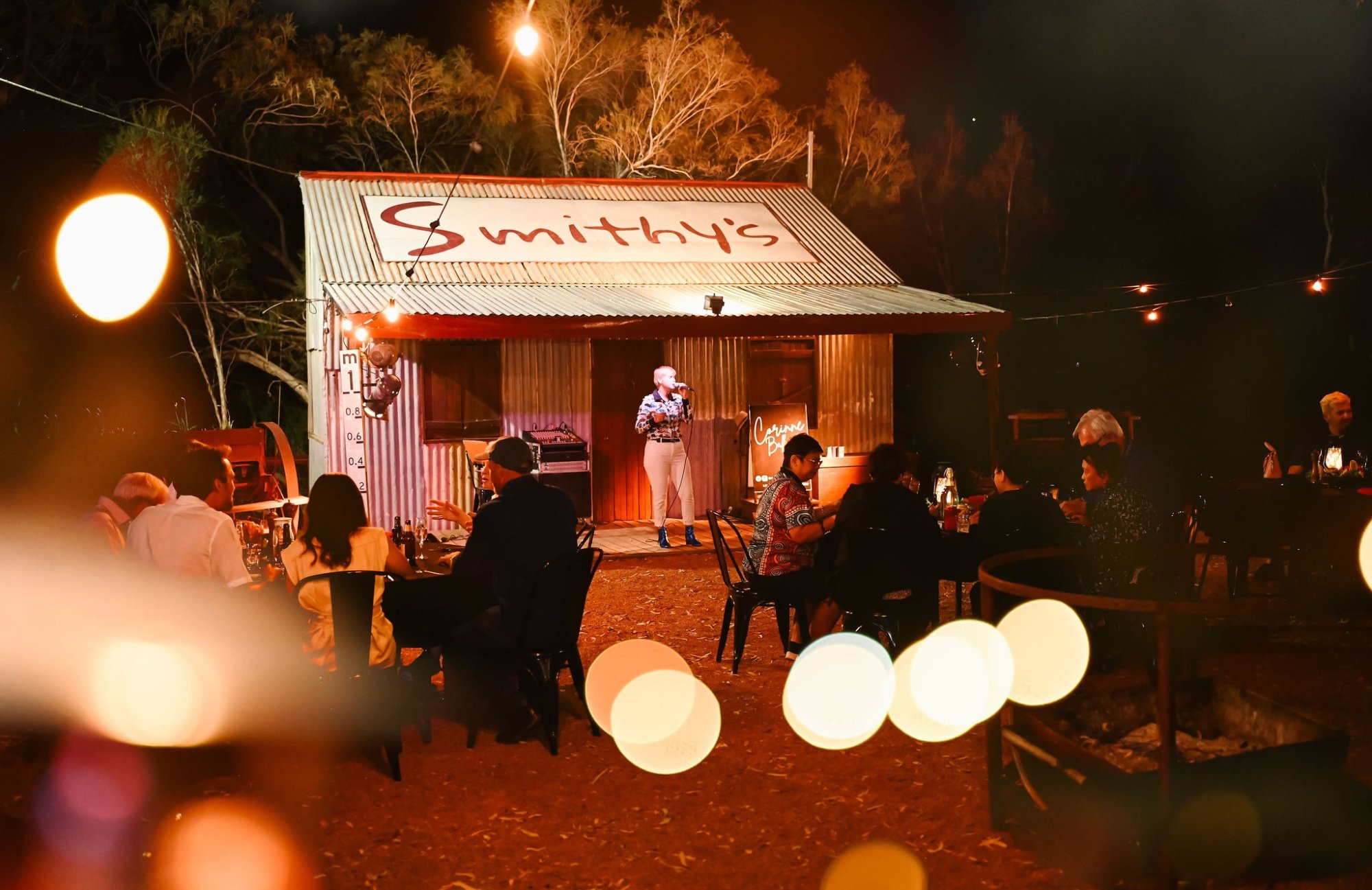 A rustic corrugated iron venue called 'Smithy's' hosts an evening entertainment event with a live