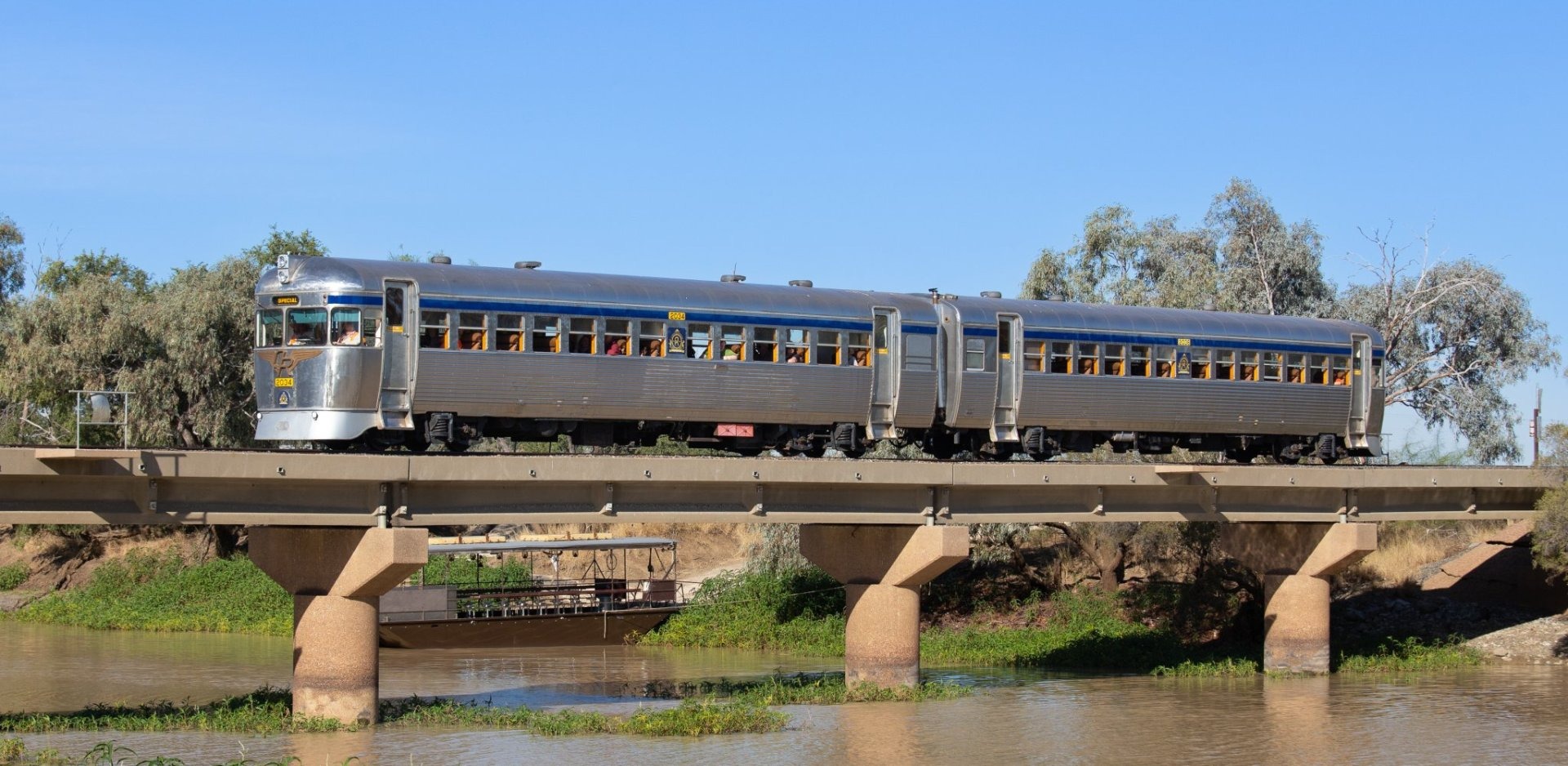 A vintage streamliner passenger train with silver and blue art deco styling crosses a concrete