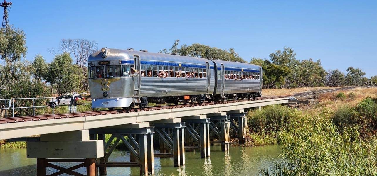 A vintage streamliner passenger train with silver and blue livery crosses a concrete bridge over