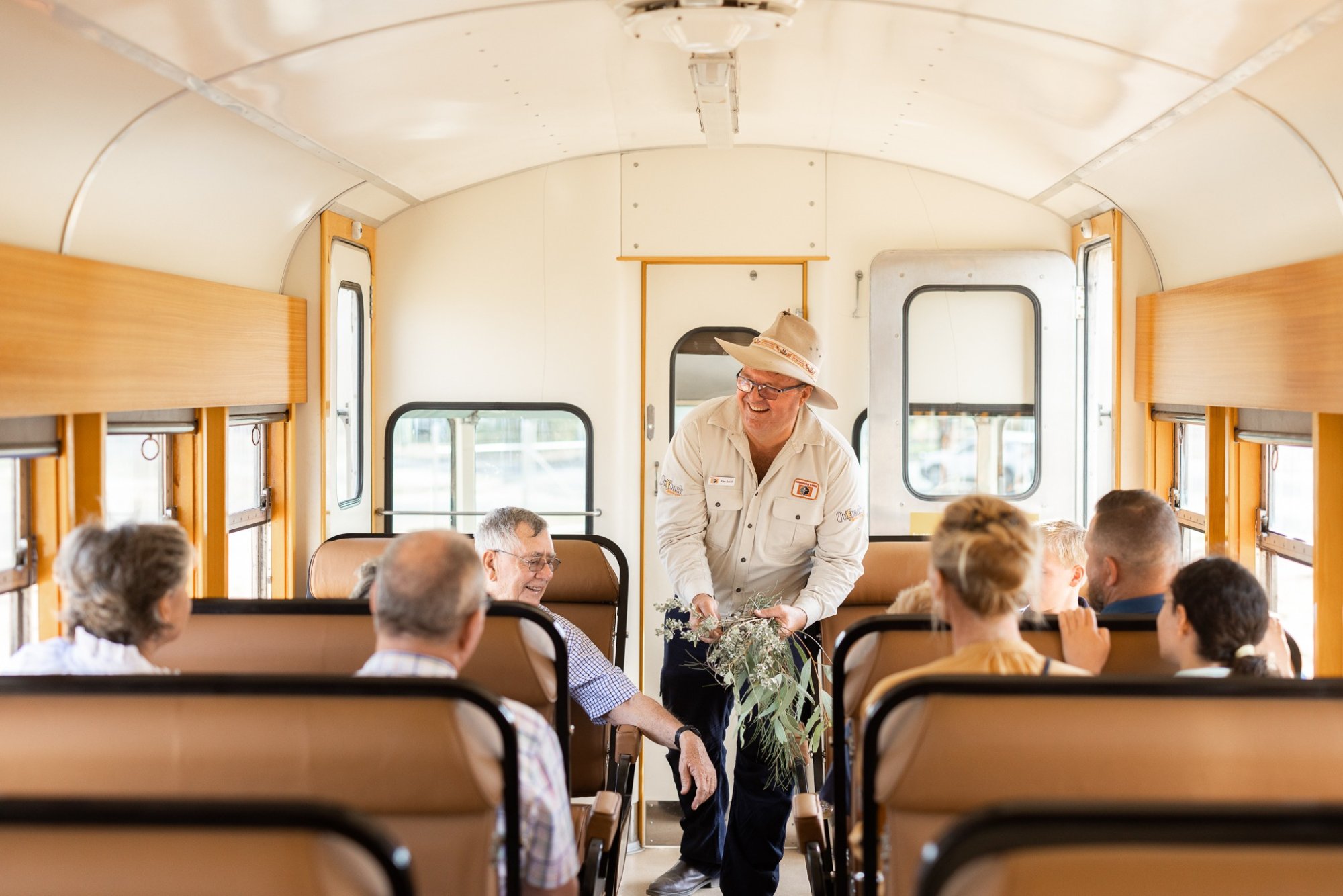 Tour Guide Presenting on Vintage Bus Interior A tour guide in khaki uniform and straw hat engages passengers aboard a vintage-style bus