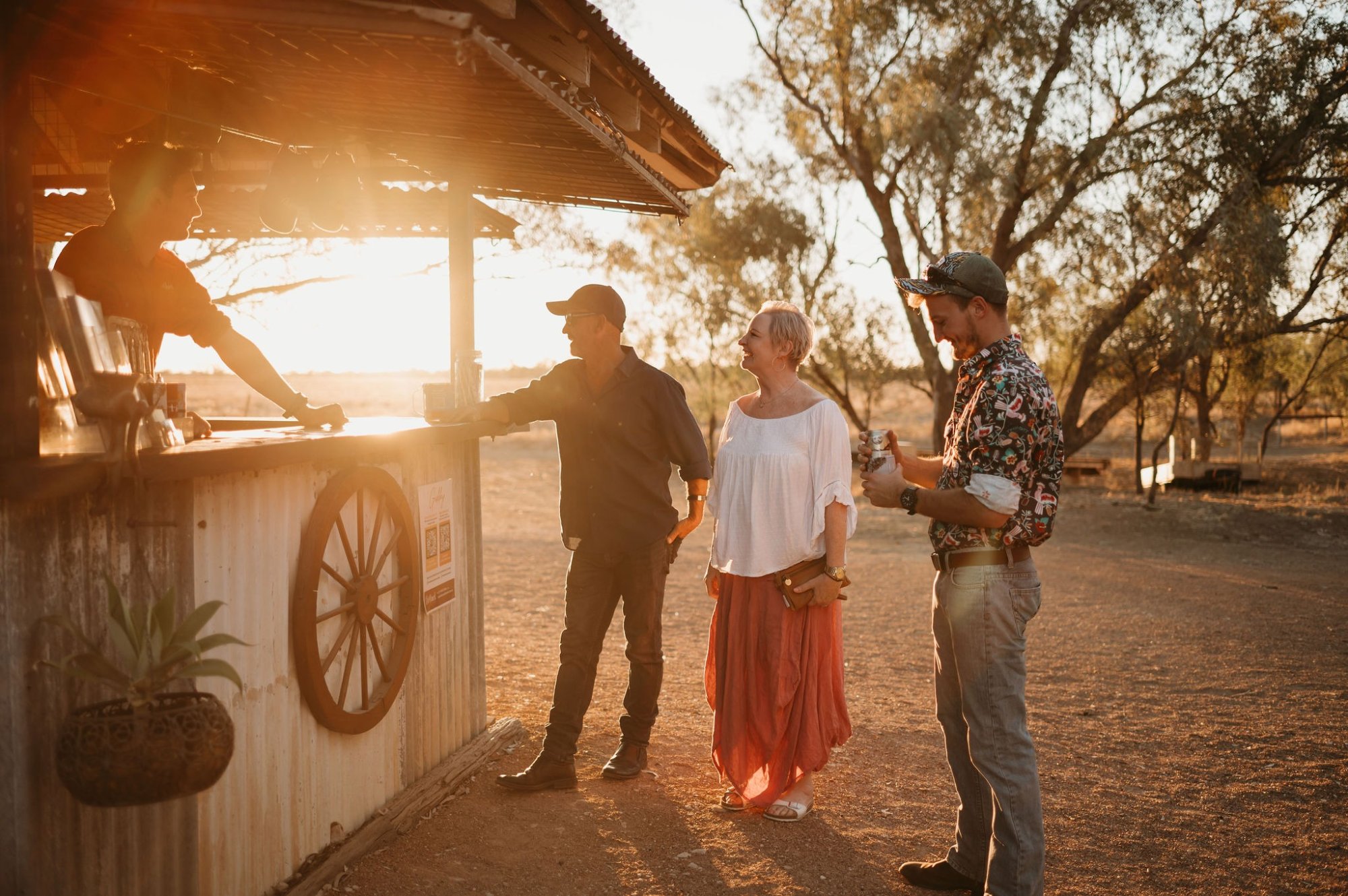 A group of three visitors interact with a ranch worker at a rustic western-style station during