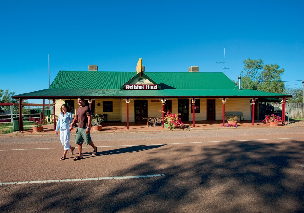 A charming outback hotel with distinctive green metal roof and red pillars, featuring a couple