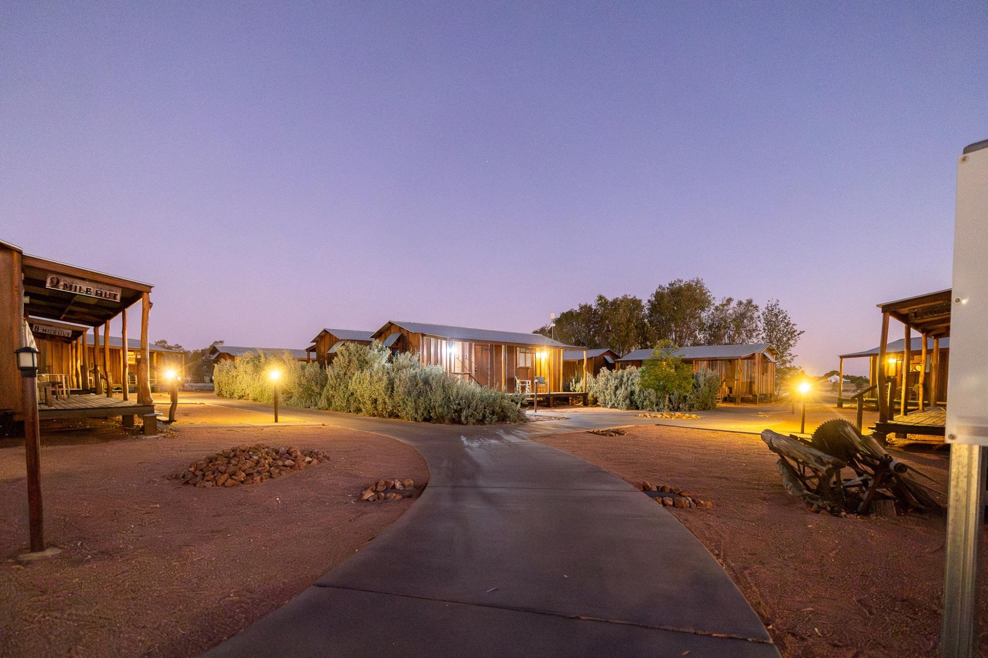 An illuminated Old West-style settlement at dusk, featuring rustic wooden buildings with period
