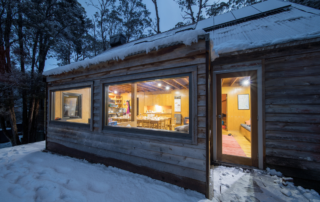 A rustic wooden cabin nestled among tall eucalyptus trees, illuminated from within during twilight